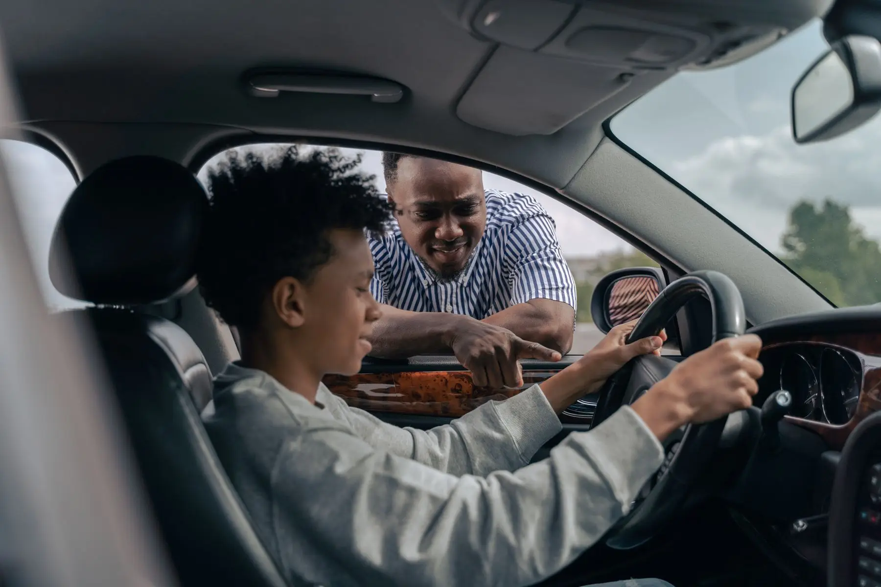 Un jeune conducteur au volant écoute les conseils d'un homme penché à la portière.