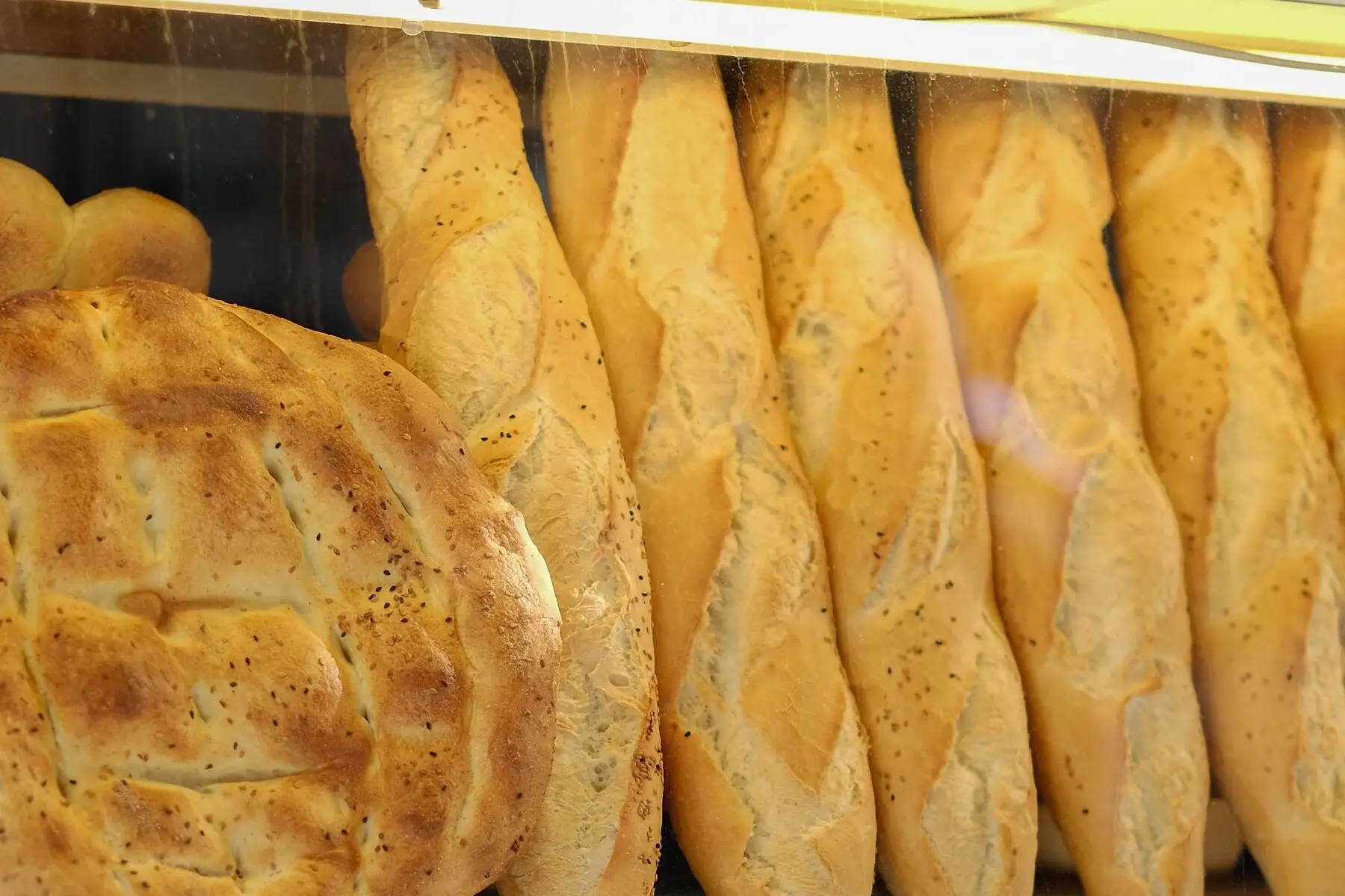 Baguettes dorées et pain rond alignés derrière la vitrine d'une boulangerie.