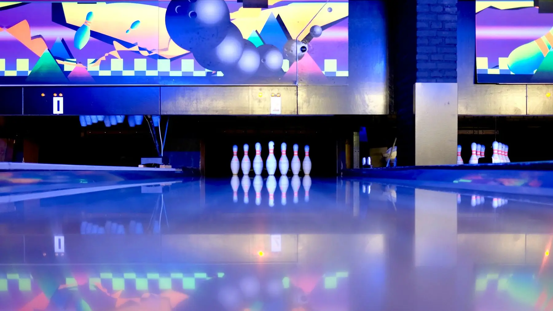 Quilles alignées au bout d'une piste de bowling, sous une fresque aux couleurs néon.