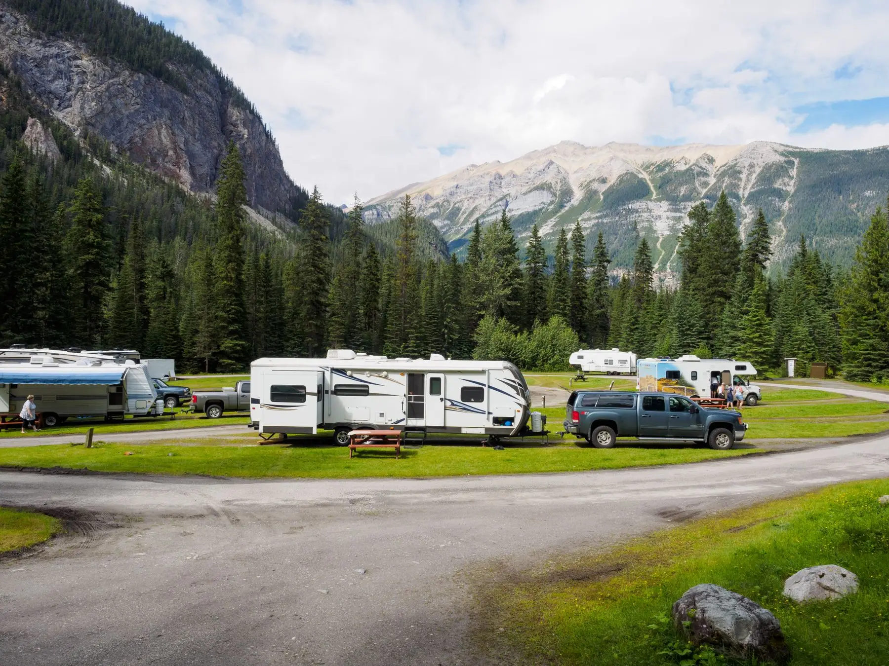 Terrain de camping en montagne, caravanes garées sur des emplacements herbeux bordés de sapins.