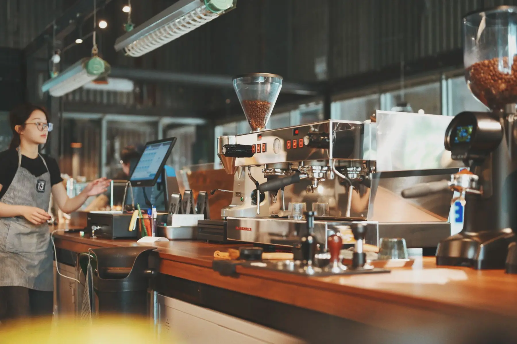 Barista derrière le comptoir en bois d'un café, près d'une machine à expresso.