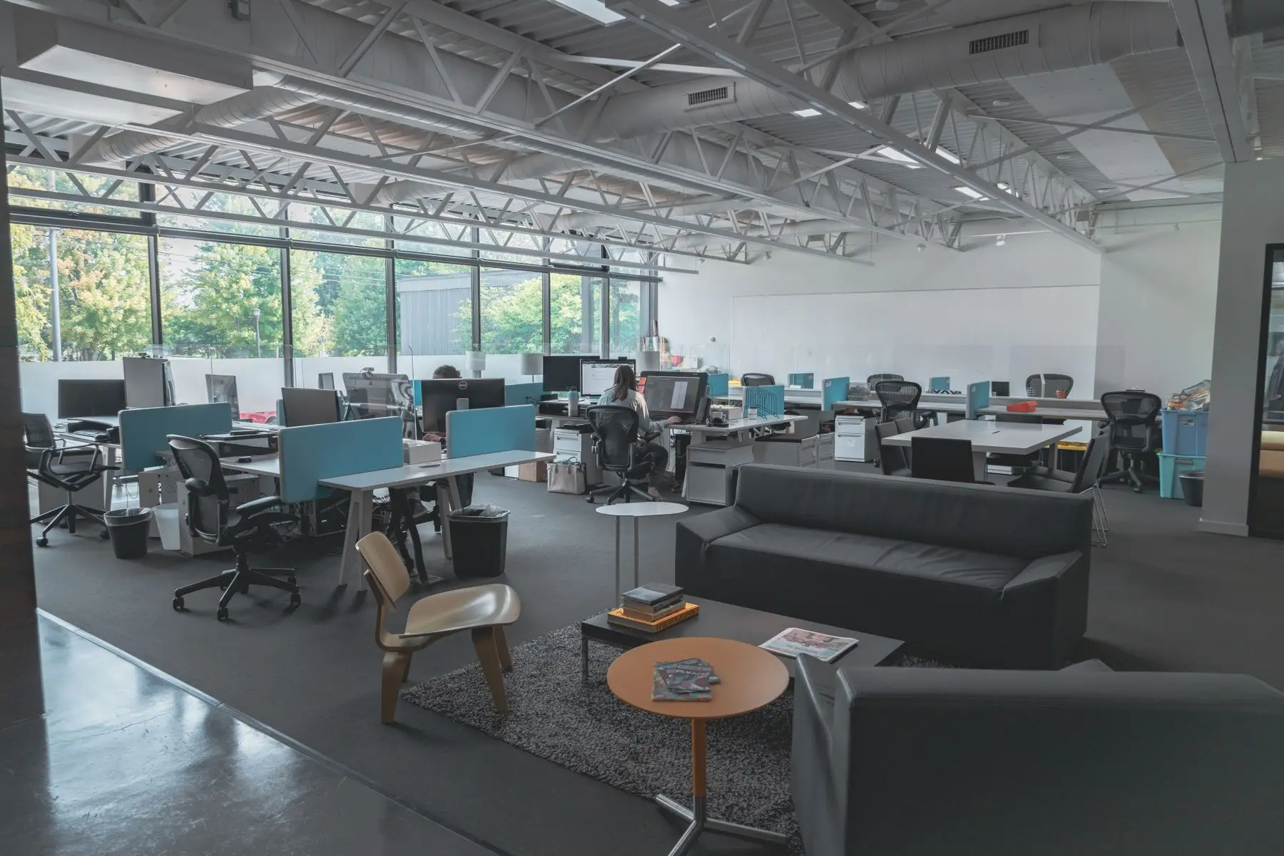 Un vaste plateau de bureaux ouvert sous une charpente métallique, avec un coin salon devant.