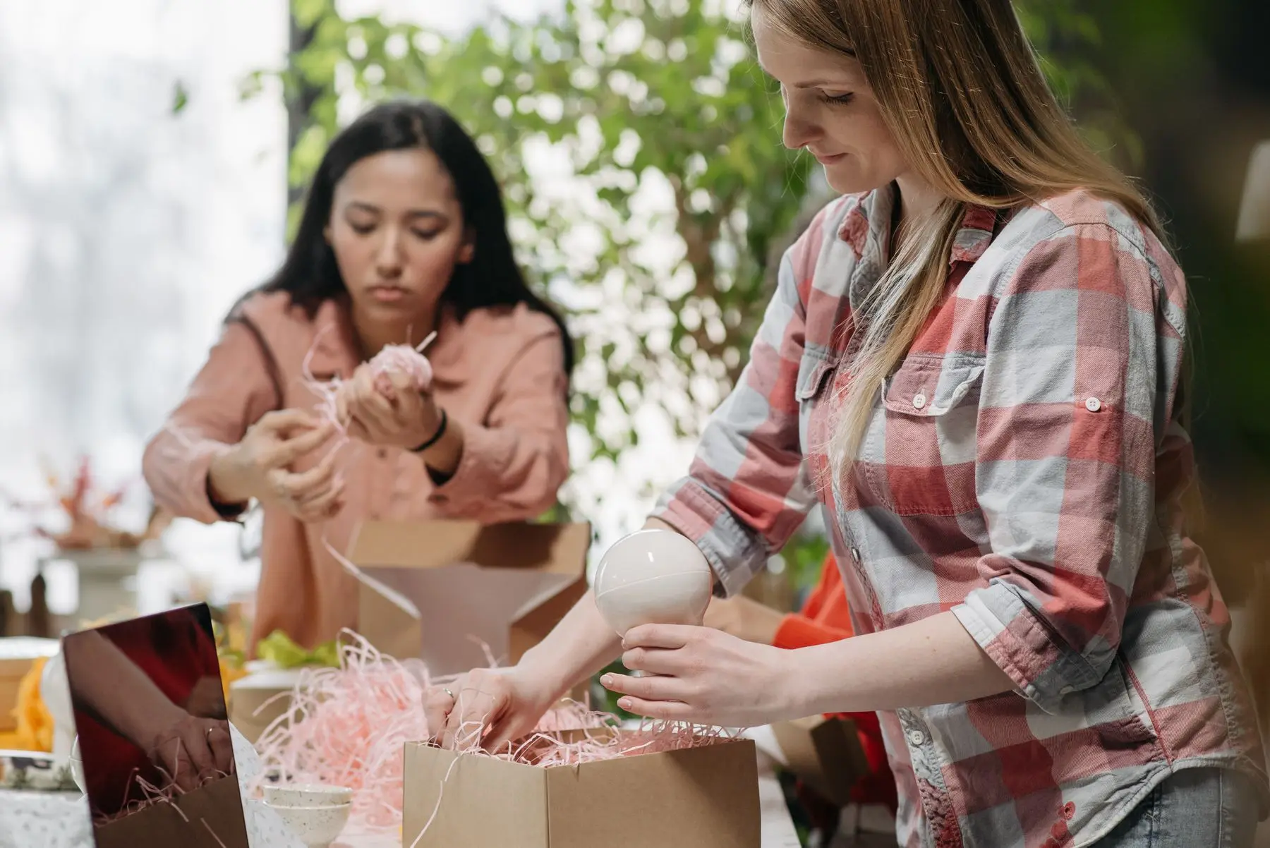 Des femmes emballent des objets en céramique dans des cartons garnis de papier frisé.