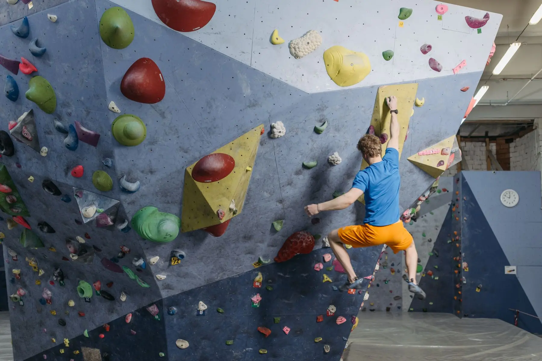 Un grimpeur en tee-shirt bleu progresse sur un mur de bloc aux prises colorées.