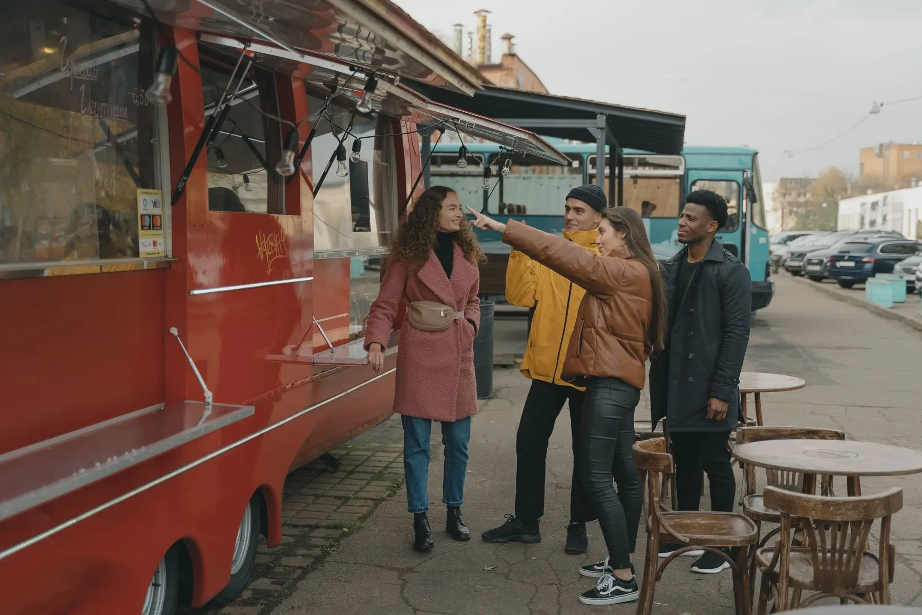 Un groupe d'amis choisit au comptoir d'un food truck rouge garé dans une rue.