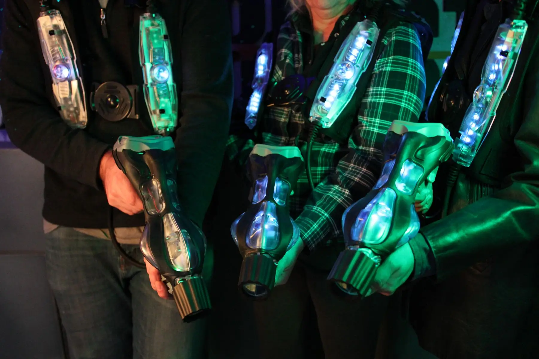 Joueurs équipés de gilets lumineux tenant leurs pistolets de laser game, en lumière verte.