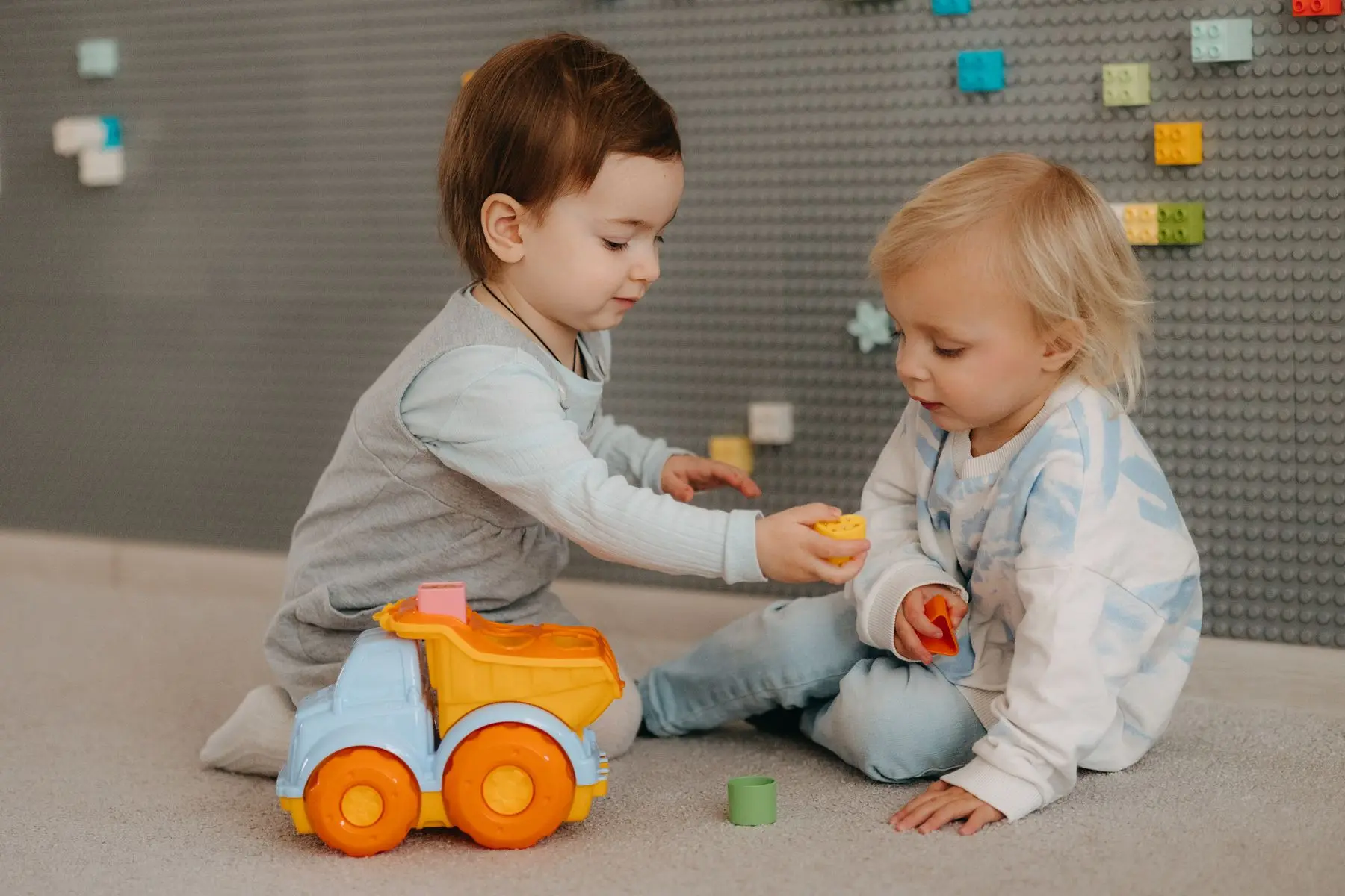 Deux tout-petits jouent avec un camion sur le tapis d'une salle de jeux.