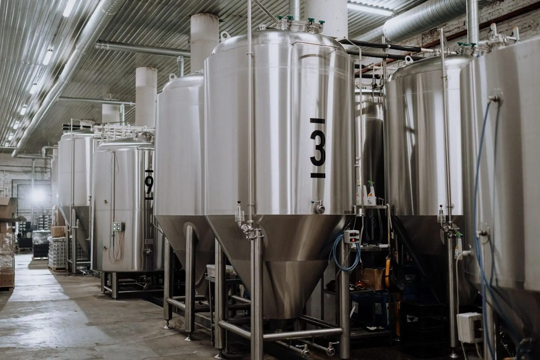 Cuves de fermentation en inox alignées dans le hall d'une brasserie.
