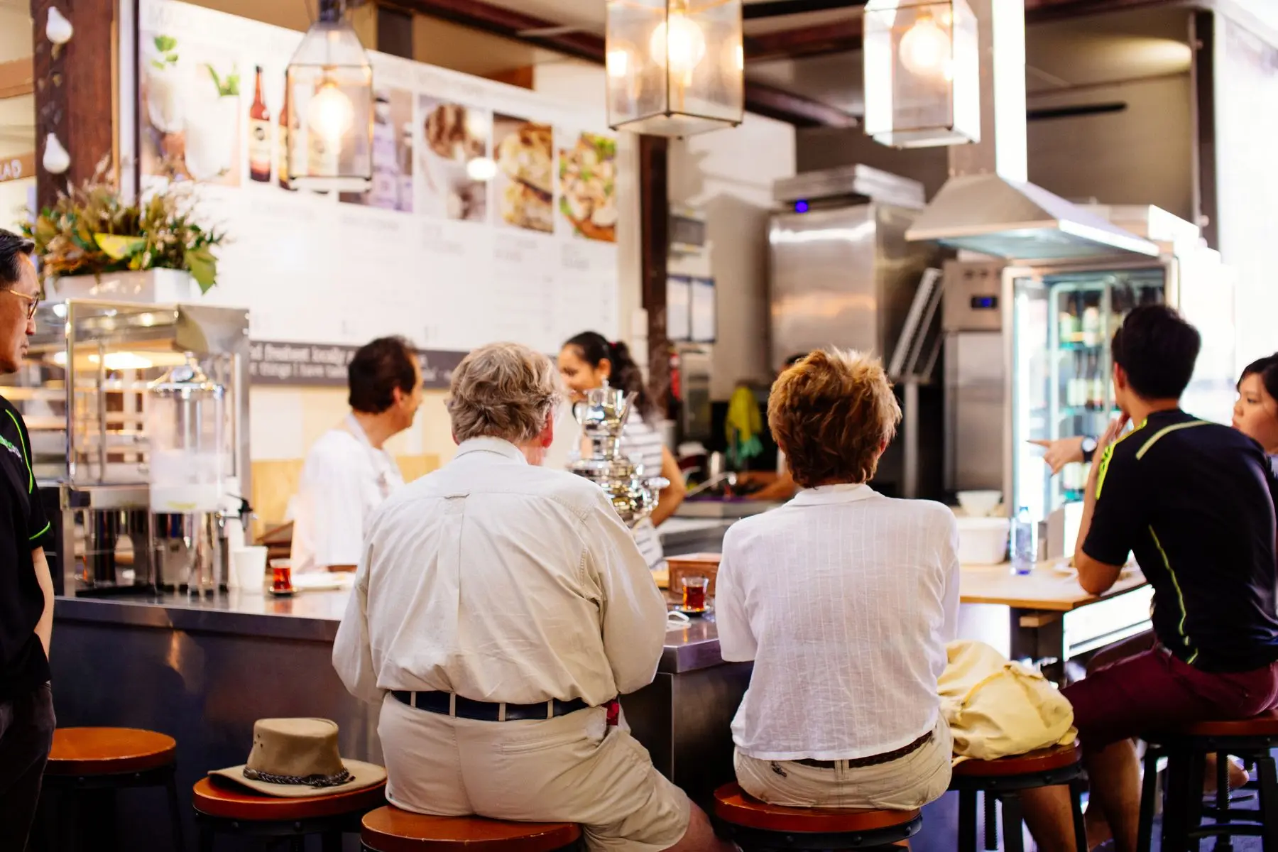Clients assis de dos au comptoir d'un restaurant, face à la cuisine ouverte.
