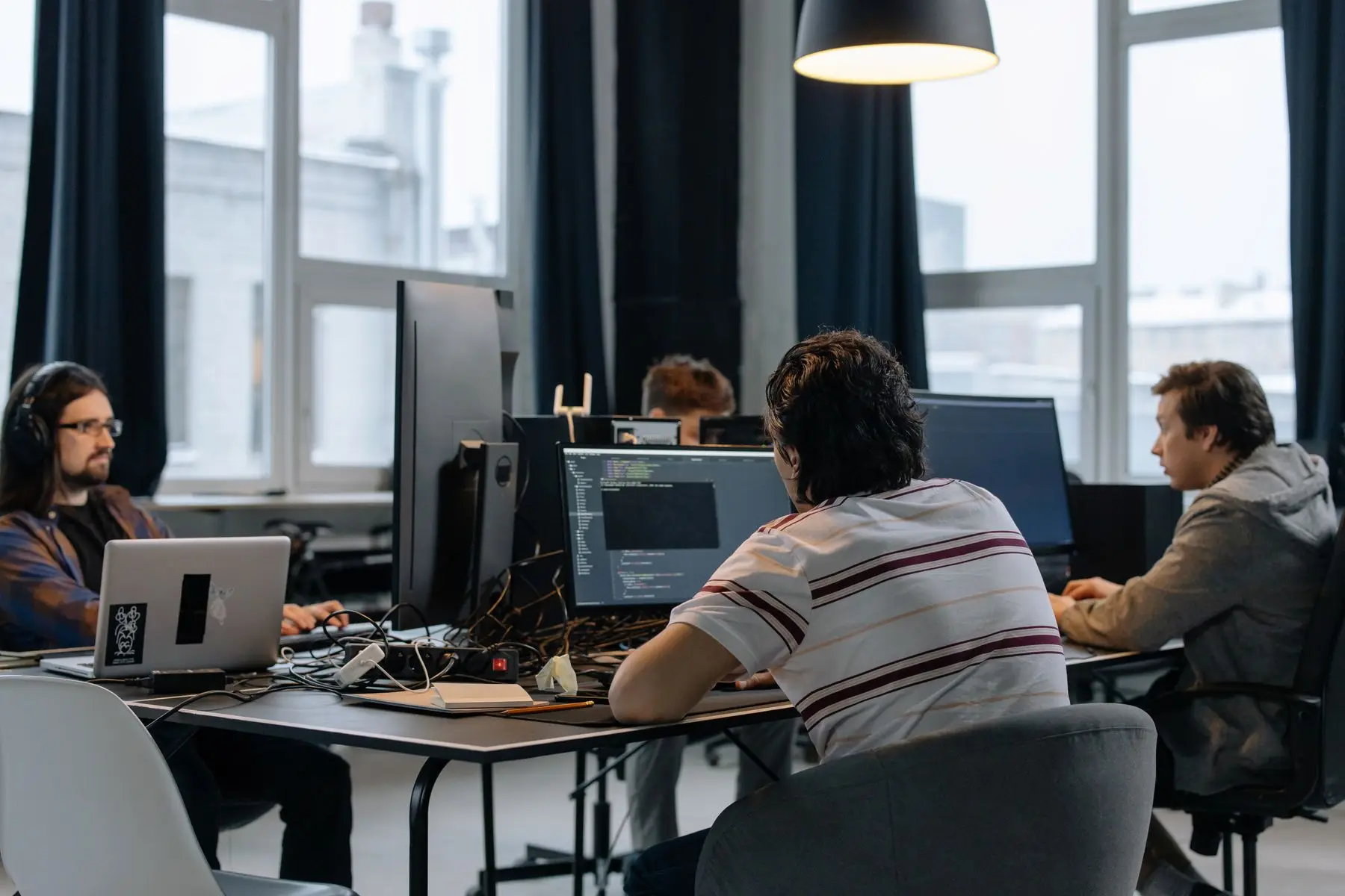 Une équipe travaille face à des écrans de code dans un bureau aux grandes fenêtres.