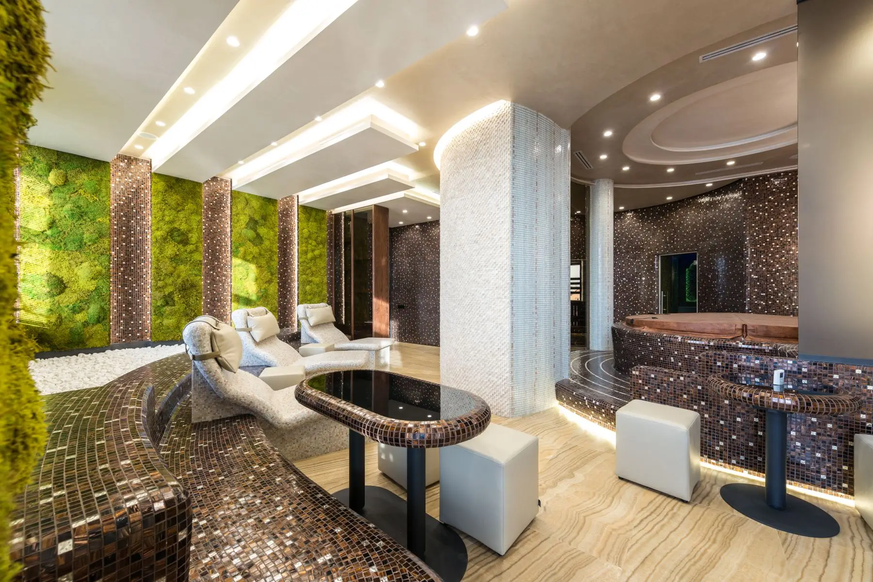 Espace détente d'un spa aux murs de mosaïque, avec transats blancs et bain à remous.